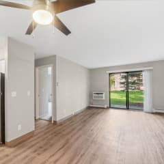 an empty living room with a refrigerator and a ceiling fan