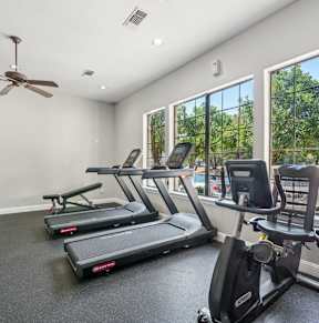 a fitness center with cardio equipment and large windows