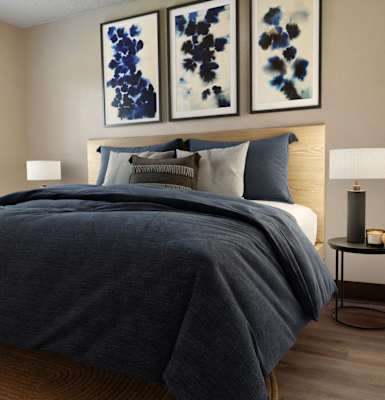 A bedroom with a large bed and two blue abstract paintings on the wall.