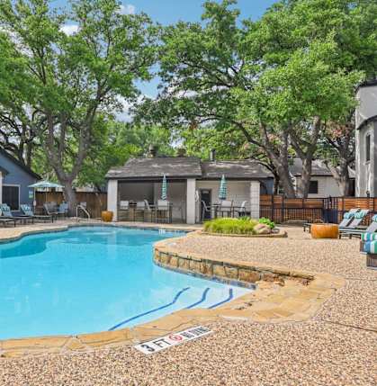 A pool surrounded by trees and chairs.