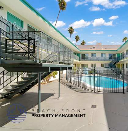 A pool is surrounded by a fence and a building with a balcony.