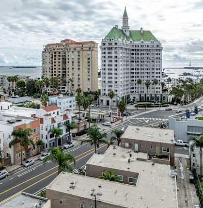 A cityscape with a mix of modern and older buildings, palm trees, and a cloudy sky.