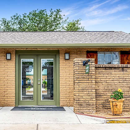 A brick building with a green door and windows with orange curtains.