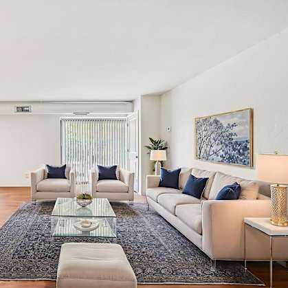 A living room with a white couch, a glass coffee table, and a rug.