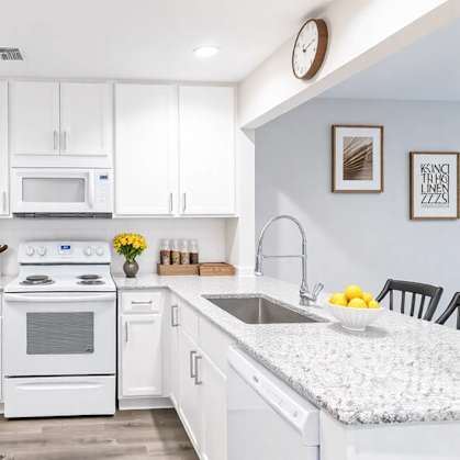 A white kitchen with a refrigerator, oven, microwave, and sink.