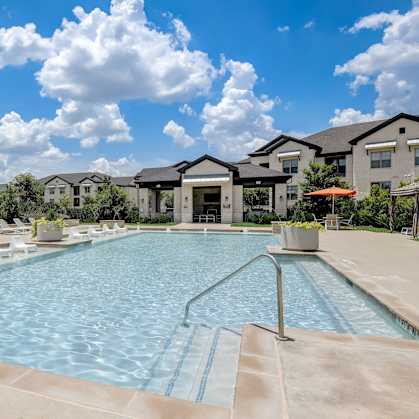 A large swimming pool surrounded by lounge chairs and buildings in the background.