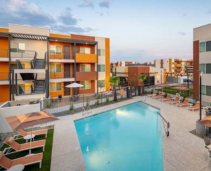 A swimming pool surrounded by lounge chairs and umbrellas in a residential area.