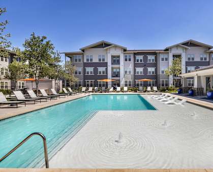 a swimming pool with lounge chairs and umbrellas in front of an apartment building