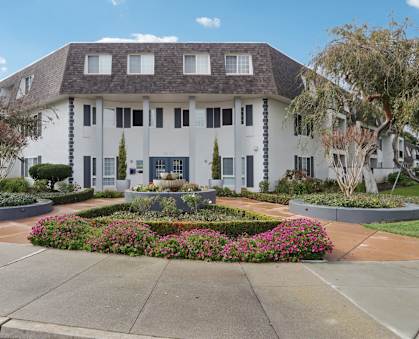 A white building with a grey roof and a garden in front.
