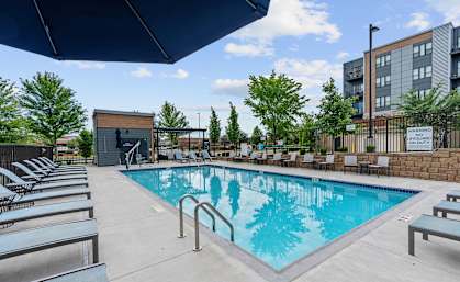 A pool with a blue tinted water and a black umbrella above it.