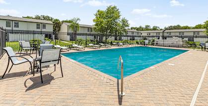 A pool surrounded by chairs and trees.