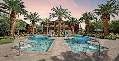 A pool surrounded by palm trees and lounge chairs.