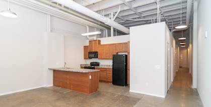 A kitchen area with a black fridge and microwave, a wooden counter, and a white wall.