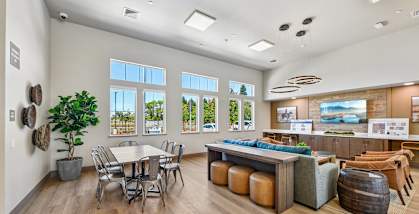 A room with a dining table and chairs, a bar with stools, and a wall with pictures and a clock.