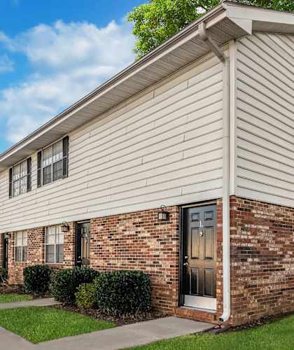 Dog-Friendly Townhomes In Spartanburg, SC - Reserve At Hillcrest - A Row Of Two-Story Townhomes With A Paved Walkway, Manicured Lawns And Hedges, And Trees.