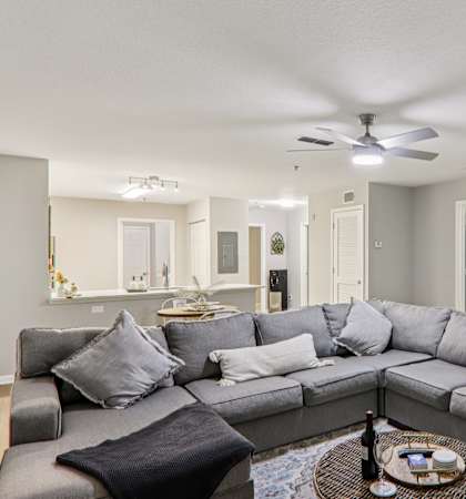 A grey sectional sofa with a black throw pillow sits in a living room with a ceiling fan and a coffee table.