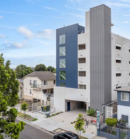 A modern building with a grey and blue exterior stands tall in the foreground of a residential area.