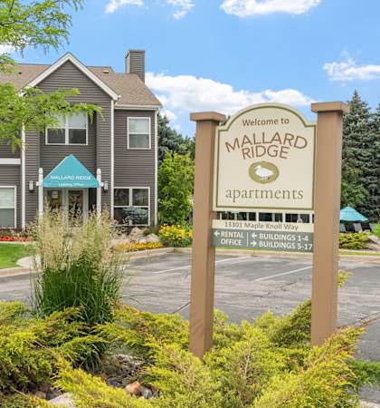 A sign welcoming people to Mallard Ridge Apartments stands in front of a building.