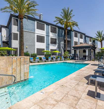 A pool surrounded by lounge chairs and umbrellas in front of a building.