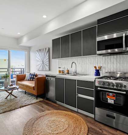a kitchen with dark cabinets and white countertops and a sliding glass door leading to a balcony at The Fairfax Flats Apartments, Los Angeles, CA, 90019