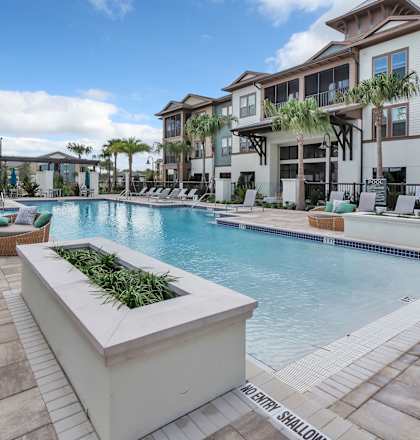Outdoor pool with flower planters, and large circular lounge chairs near apartment building