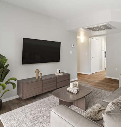 A living room with a grey couch, a coffee table, and a flat screen TV mounted on the wall.