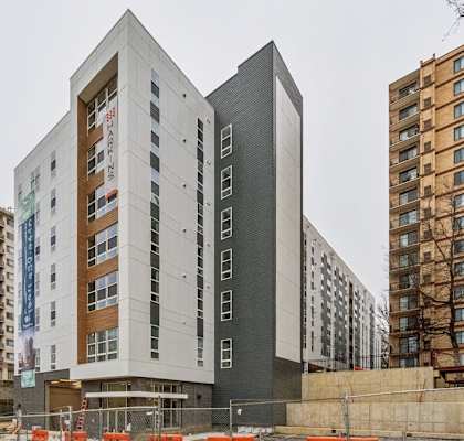 A modern building with a mix of white and dark grey panels stands in front of a construction site.