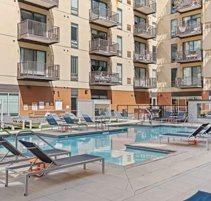 A large outdoor pool area with sun loungers and apartment buildings in the background.