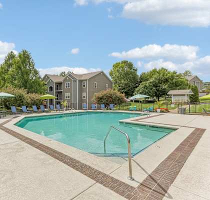 A swimming pool surrounded by a concrete patio and lawn chairs.
