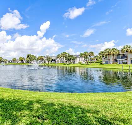 a large pond with a fountain in the middle of a grassy field at Waterford Park Apartment Homes, LLC, Lauderhill