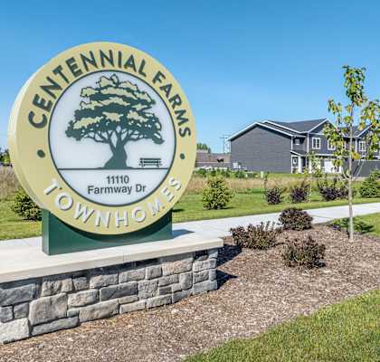 A sign for Centennial Farms Townhomes stands in front of a building.