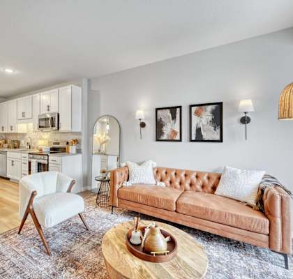 A modern living room with a brown leather couch and a white chair at Lochner Apartments, White Bear Lake, MN,  55110