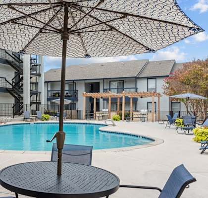 A black umbrella is over a table in the middle of a pool.