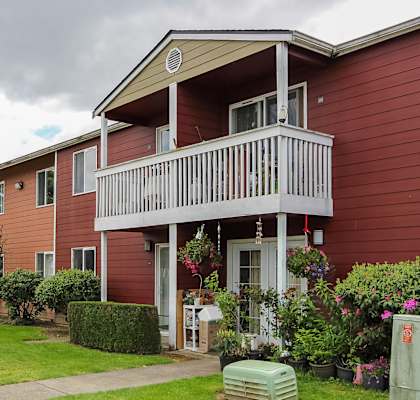 A red building with a balcony and a small garden in front.