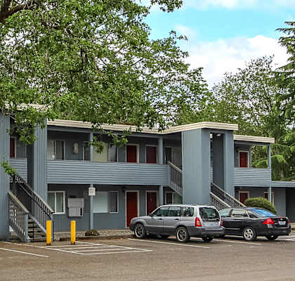 A grey building with a red door and a tree in front.