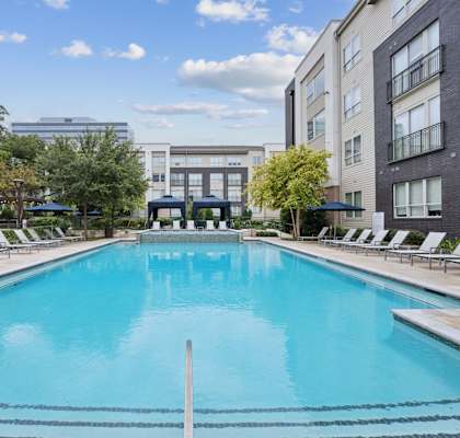 A large swimming pool in a residential area with lounge chairs around it.