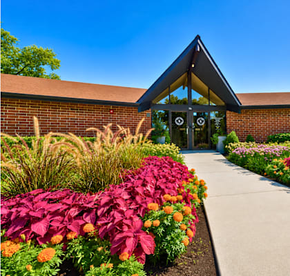 A building with a triangular roof is surrounded by a garden with colorful flowers.