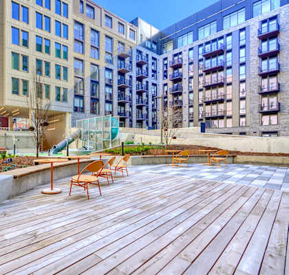 A wooden deck with chairs and a slide in the middle of a courtyard surrounded by buildings.