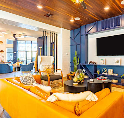 A living room with a yellow couch and a flat screen TV mounted on the wall.