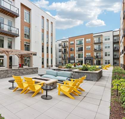 A patio with yellow chairs and tables is surrounded by apartment buildings.