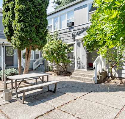 a picnic table and trash can sit on a patio in front of a gray building