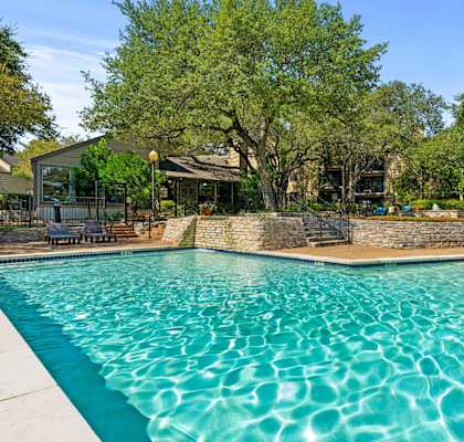 A swimming pool surrounded by trees and a stone wall.