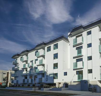 A modern white building with balconies and a blue sky in the background.