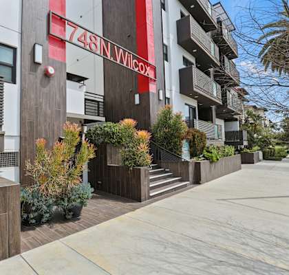 an apartment building with a sidewalk and plants in front of it