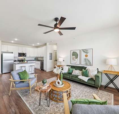 An image of a kitchen, living room, with a green couch, two accent chairs, and a wooden coffee table. 