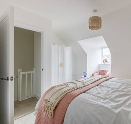 A bedroom with a bed covered in a white sheet and a pink blanket.