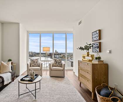 A living room with a grey couch, a coffee table, and a large window with a view of the city.