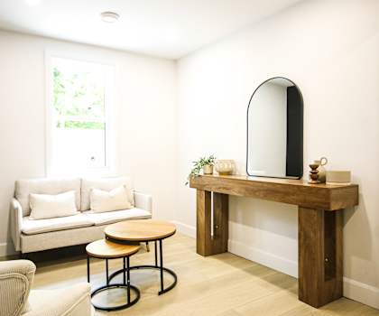 A living room with a white couch, a wooden table, and a round chair.