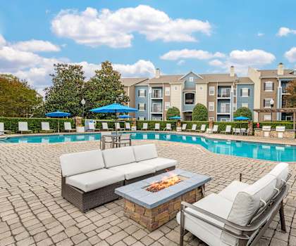 A poolside area with a couch, chairs, and a fire pit.