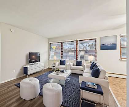 A living room with a white couch, a blue ottoman, and a television.